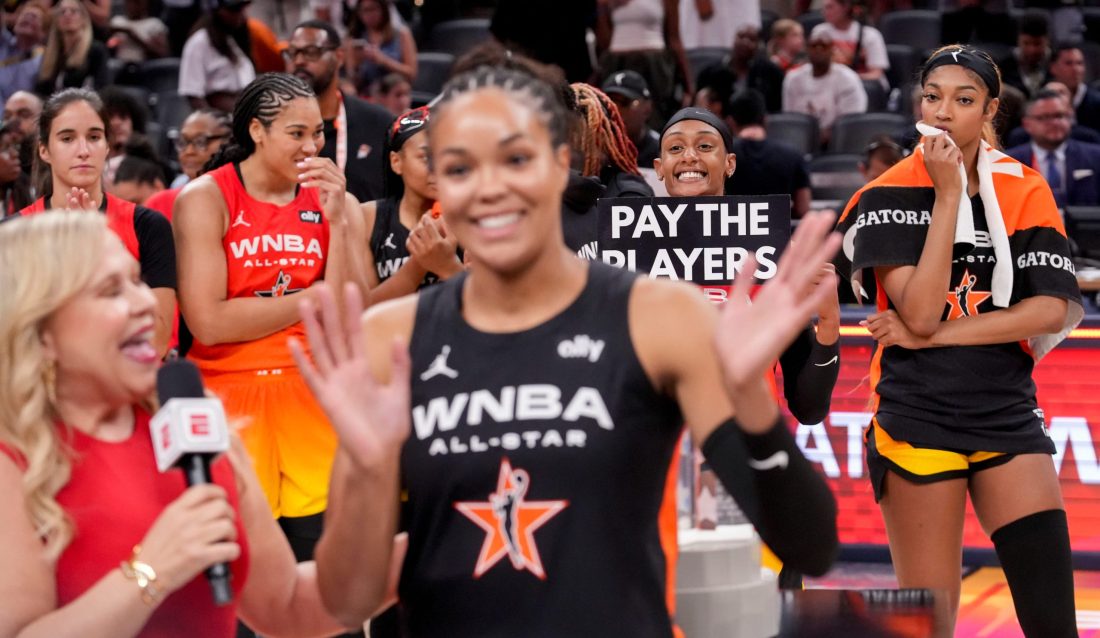 Washington Mystics' Brittney Sykes (20) holds a sign as Minnesota Lynx's Napheesa Collier (24) is interviewed Saturday, July 19, 2025, during the WNBA All-Star Game at Gainbridge Fieldhouse in Indianapolis.