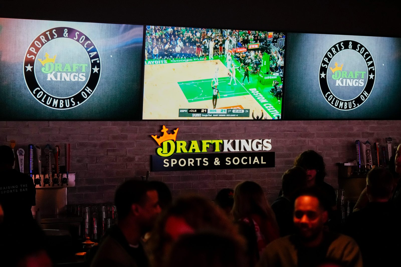 Sports are shown on TVs behind a bar as guests enjoy the grand opening of DraftKings Sports & Social in Ohio.