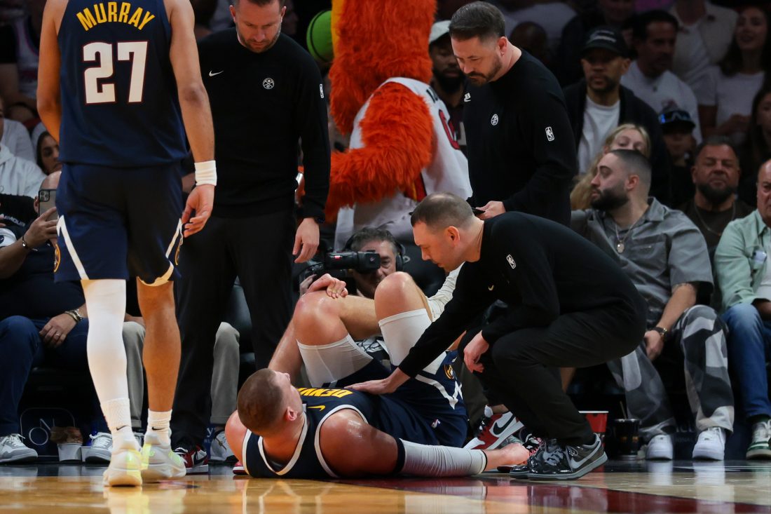 Dec 29, 2025; Miami, Florida, USA; Denver Nuggets center Nikola Jokic (15) grabs his left knee as head coach David Adelman approaches him after an injury against the Miami Heat during the second quarter at Kaseya Center. Mandatory Credit: Sam Navarro-Imagn Images