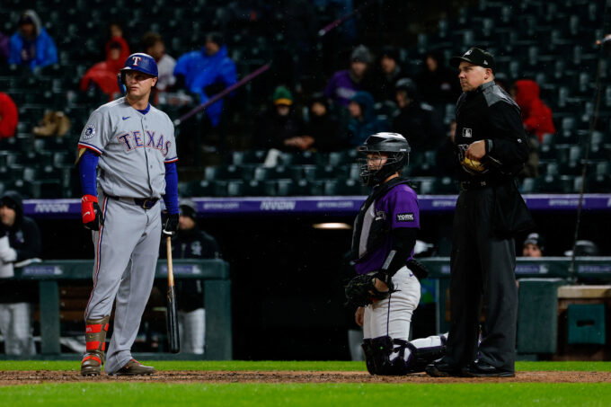 May 18, 2026; Denver, Colorado, USA; Texas Rangers pinch hitter Joc Pederson (3) watches the video board with Colorado Rockies catcher Hunter Goodman (15) and home plate umpire John Tumpane (74) after challenging a pitch call in the seventh inning at Coors Field. Mandatory Credit: Isaiah J. Downing-Imagn Images
