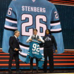 Jun 26, 2026; Buffalo, New York, USA; Ivar Stenberg puts on a San Jose Sharks sweater beside NHL commissioner Gary Bettman after being selected with the second pick in the first round of the 2026 NHL Draft at KeyBank Center. Mandatory Credit: Timothy T. Ludwig-Imagn Images
