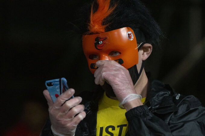 Apr 24, 2021; Baltimore, Maryland, USA; A fan wearing a Baltimore Orioles mask looks towards their phone during the game against the Oakland Athletics at Oriole Park at Camden Yards. Mandatory Credit: Tommy Gilligan-USA TODAY Sports