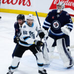 Jan 24, 2025; Winnipeg, Manitoba, CAN; Winnipeg Jets forward David Gustafsson (19) jostles for position with Utah Hockey Club forward Kevin Stenlund (82) in front of Winnipeg Jets goalie Connor Hellebuyck (37) during the third period at Canada Life Centre. Mandatory Credit: Terrence Lee-Imagn Images